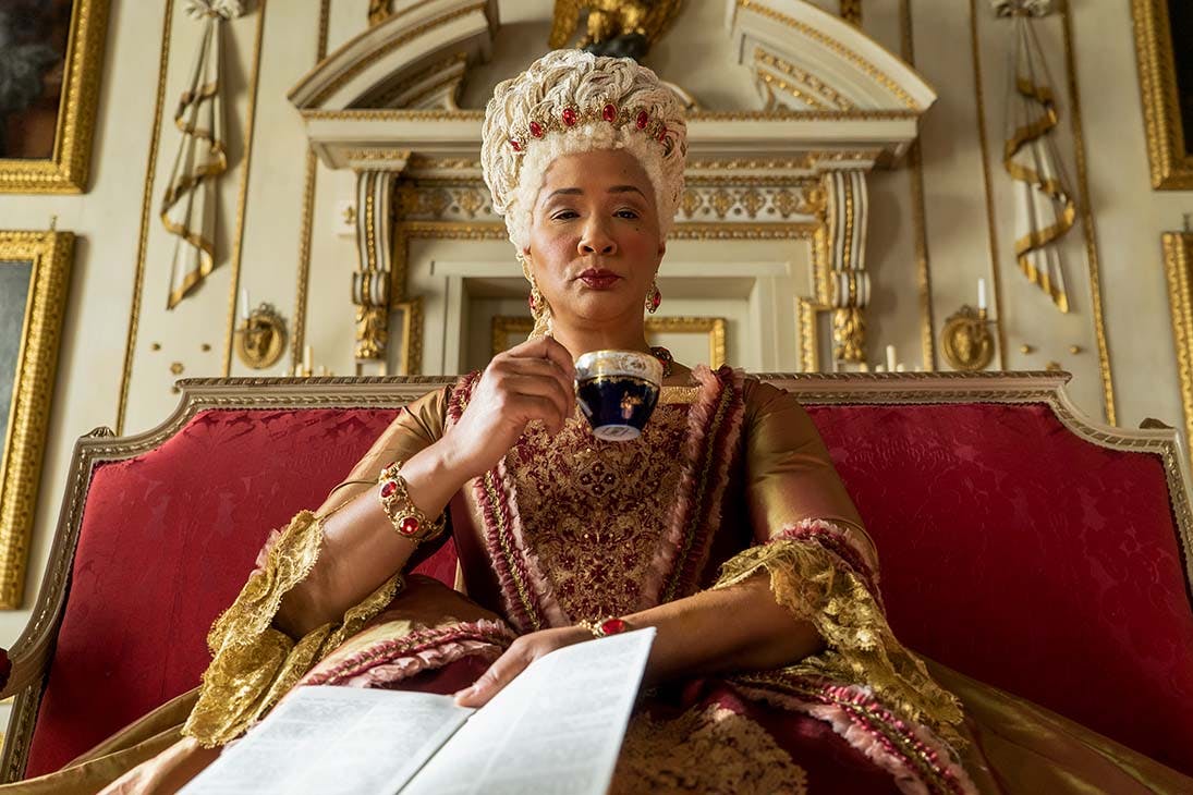 Queen Charlotte of Bridgerton holds a paper and sips a cup of tea.